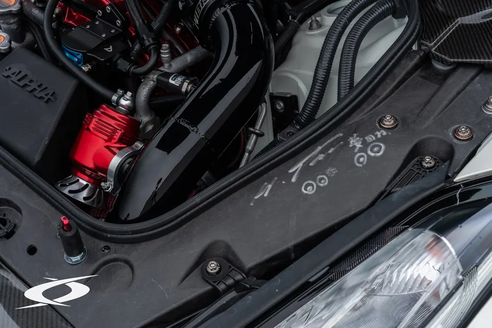 A close-up of a performance car's engine bay, showing a red blow-off valve and black intake piping.