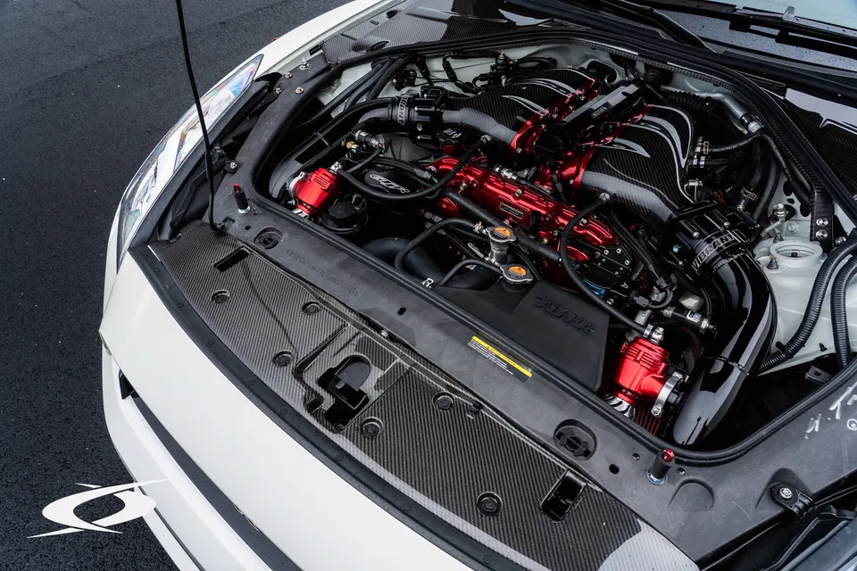 A detailed view of a Nissan GT-R's engine bay featuring a red aftermarket intake manifold and carbon fiber components.