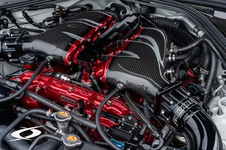 A detailed view of a custom engine bay featuring a carbon fiber intake manifold, red engine components, and performance fuel rails.