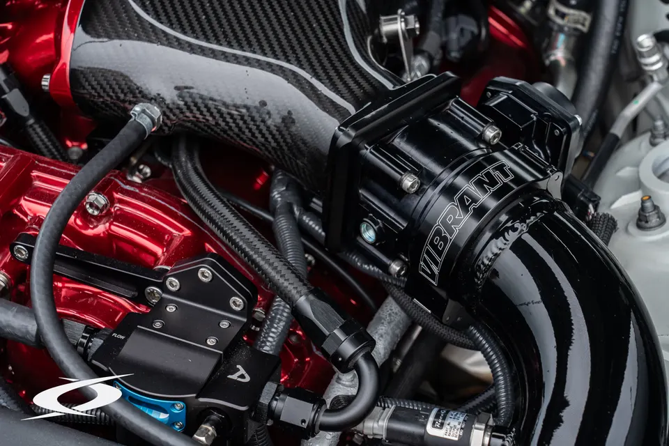 Close-up of a high-performance engine bay featuring a carbon fiber intake, Vibrant performance parts, and custom fuel system components.