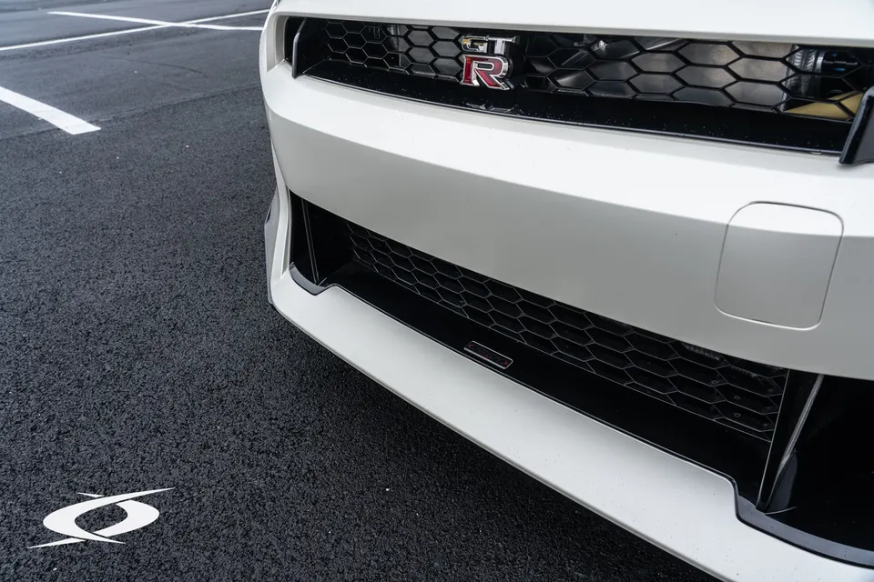 Close-up of a white Nissan GT-R's front bumper and grille, showcasing the GT-R badge and a performance intercooler.