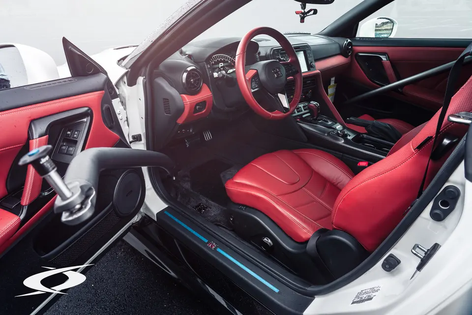 Detailed view of a Nissan GT-R interior with red leather seats, steering wheel, and a black roll bar.