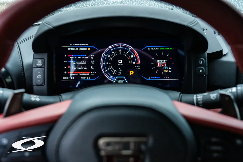 Close-up of a Nissan GT-R's digital dashboard displaying engine mode, fuel composition, oil pressure, fuel pressure, and coolant temperature.