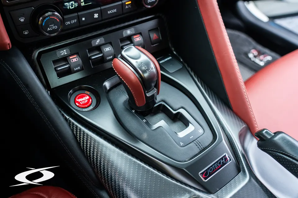 Close-up of a Nissan GT-R interior featuring a red leather shifter, carbon fiber trim, and Jotech branding.