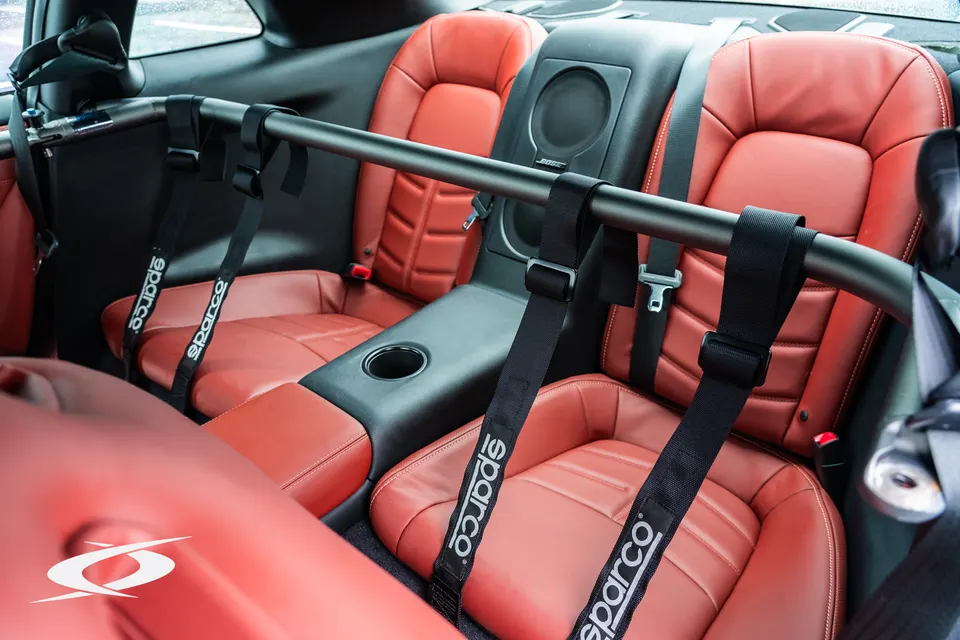 Nissan GT-R interior with red leather seats, Sparco harnesses, and a black harness bar.