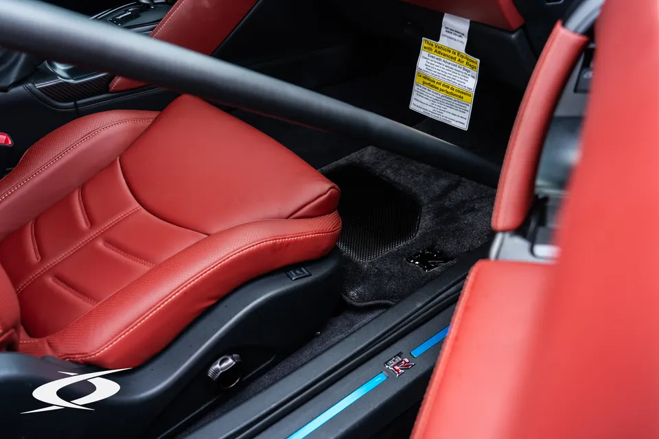 Close-up of a Nissan GT-R's red leather interior with a black roll bar and illuminated GT-R door sill.