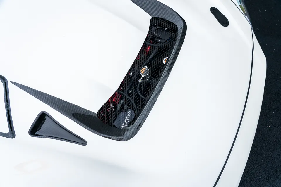 Close-up of a white car's carbon fiber hood vent revealing parts of the engine bay.