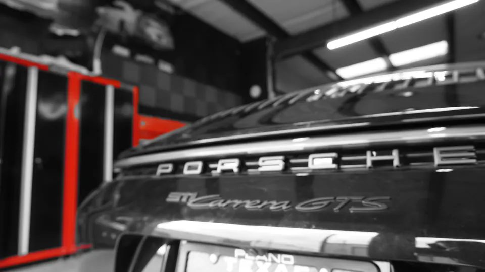 Rear view of a black Porsche 911 Carrera GTS in a shop setting with red tool cabinets in the background.