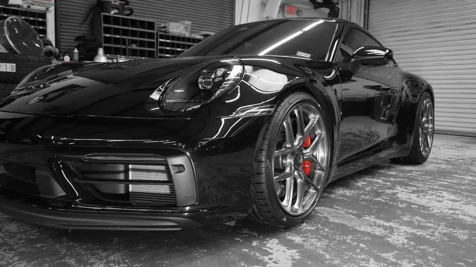 A black Porsche 911 with custom silver wheels and red brake calipers parked in a garage.