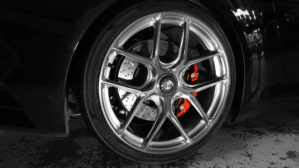 Close-up of a Porsche wheel with silver multi-spoke rims, red brake calipers, and perforated rotors.