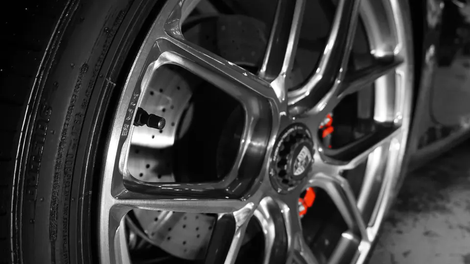 Close-up of a Porsche wheel with a performance tire and red brake caliper, showcasing the perforated rotor.