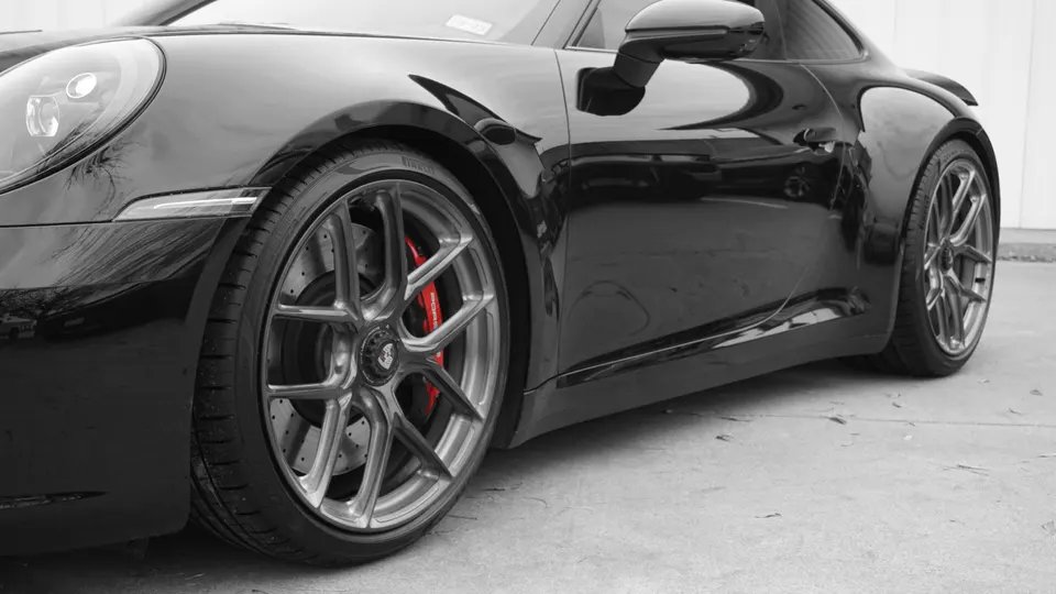 A close-up of a shiny black Porsche's front wheel, featuring multi-spoke silver wheels and bright red brake calipers.