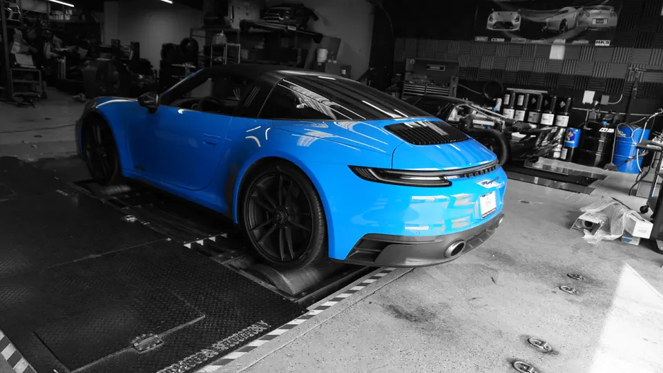 Blue Porsche 911 on a dynamometer at a performance tuning shop, ready for performance testing.