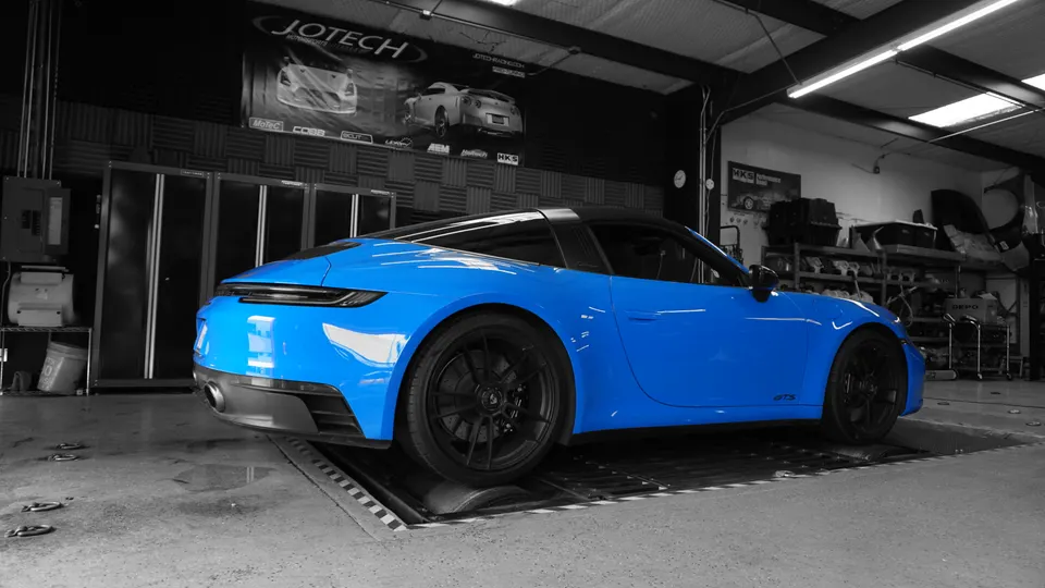 A blue Porsche 911 Targa GTS on a dynamometer in a performance tuning shop.