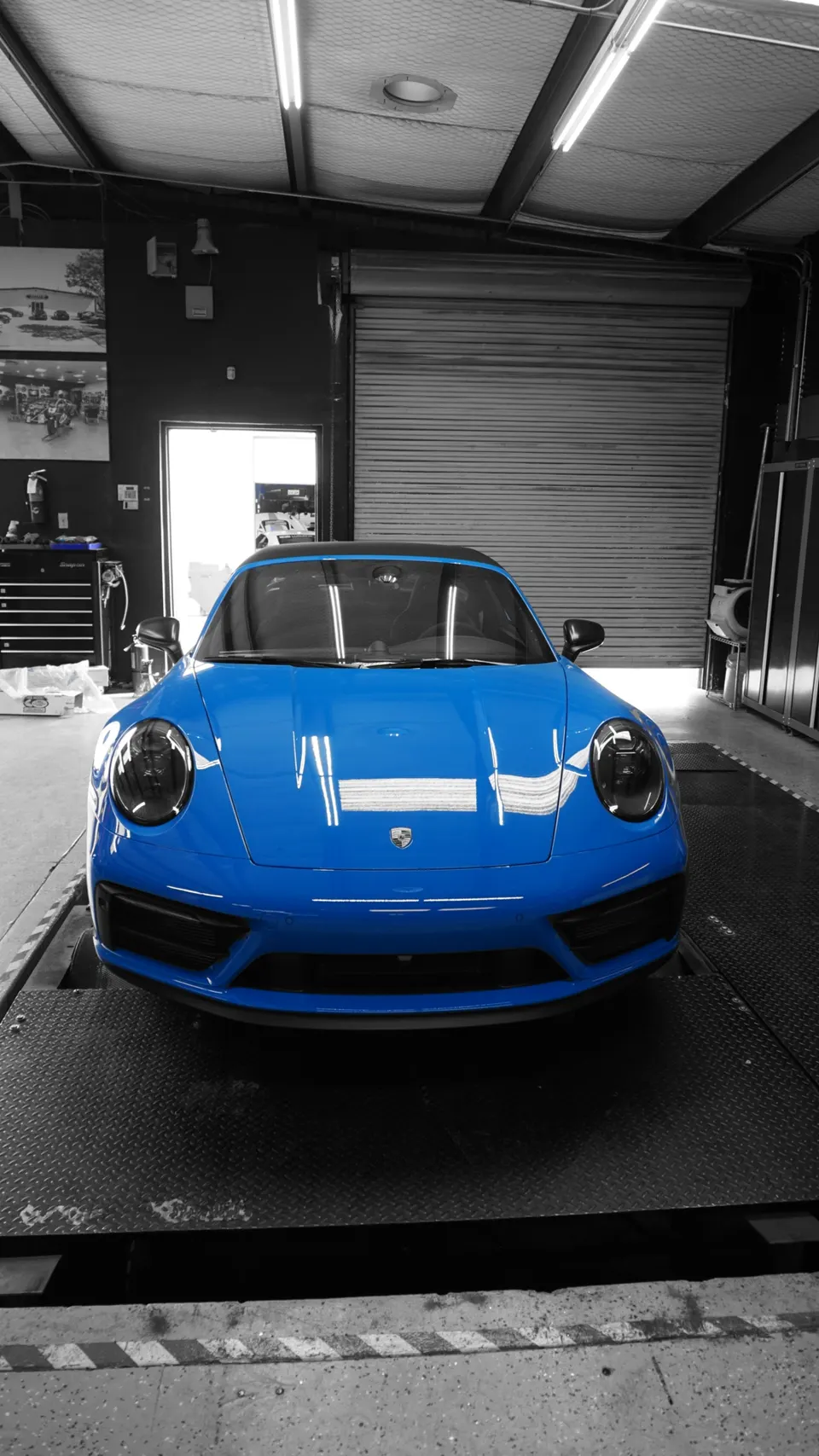 A bright blue Porsche 911 sports car parked in a performance tuning shop, viewed from the front.