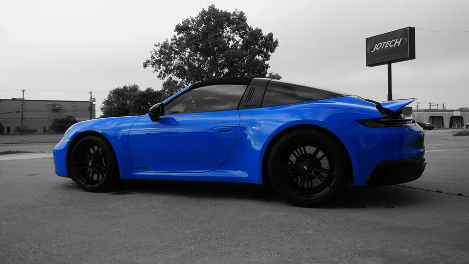 A blue Porsche 911 Targa GTS with black wheels parked outdoors in front of a Jotech sign.