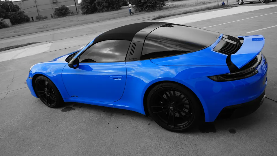 Blue Porsche 911 Targa GTS with black wheels and a black targa top parked on asphalt, showcasing its sleek design.