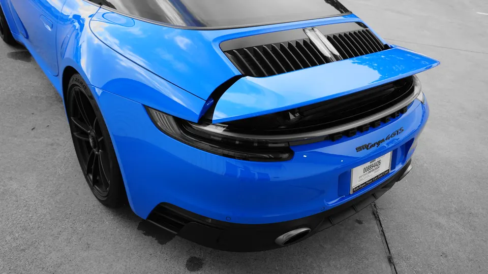 Blue Porsche 911 Targa 4 GTS rear view with active spoiler deployed, parked on concrete.