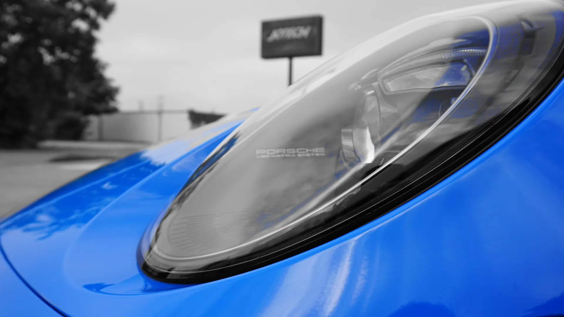 Close-up detail of a blue Porsche's headlight and front fender, with a blurred background.