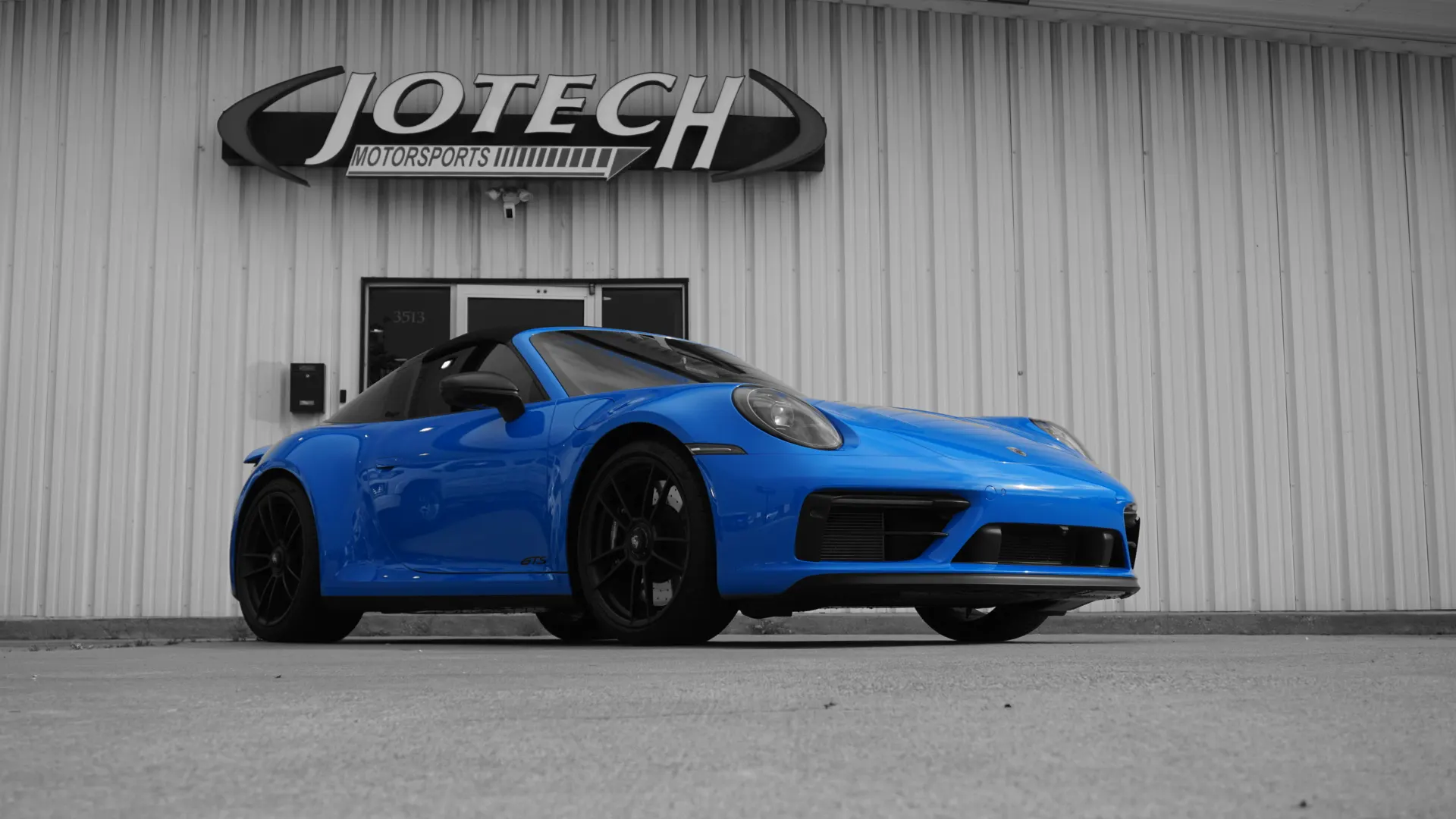 A blue Porsche 911 Targa 4S parked outside Jotech Motorsports performance tuning shop.