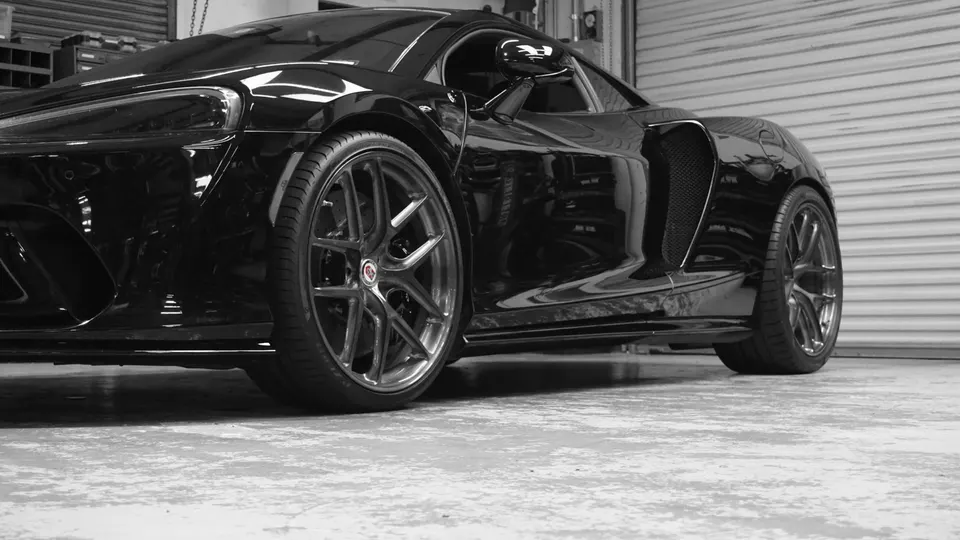 A sleek black McLaren supercar featuring custom HRE wheels, parked in a clean garage setting.