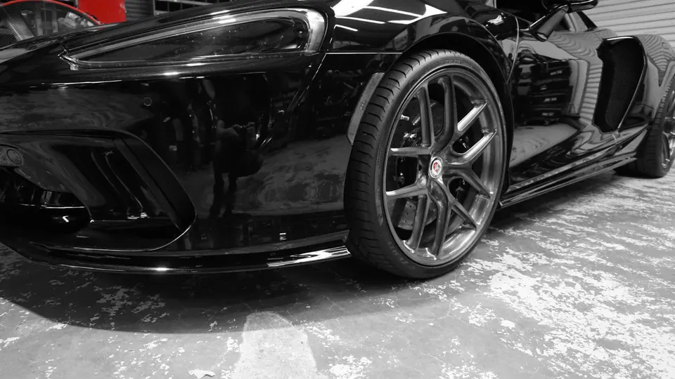 A black McLaren supercar with HRE performance wheels and tires, showcasing its sleek design in a shop setting.