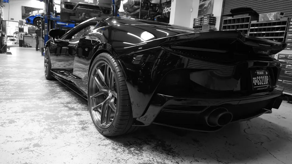Black McLaren supercar with custom wheels and aftermarket exhaust in a performance tuning shop.