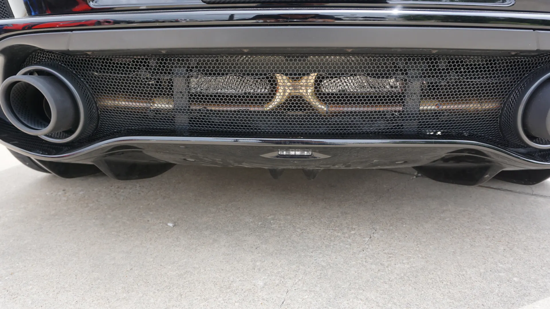 A close-up of the rear of a black sports car, showing dual exhaust tips, a honeycomb grille, and a rear diffuser.
