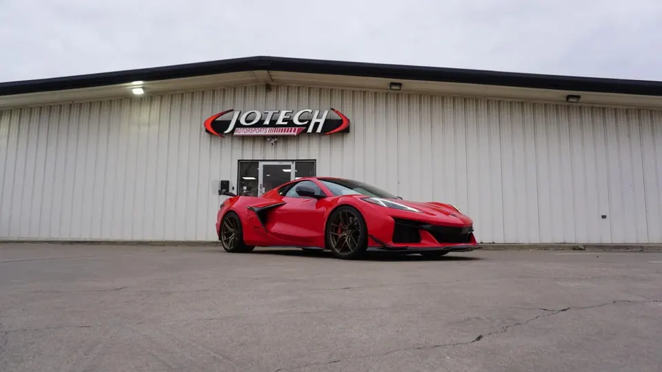 Red Corvette Z06 parked outside Jotech Motorsports building, showcasing its aggressive styling and performance stance.