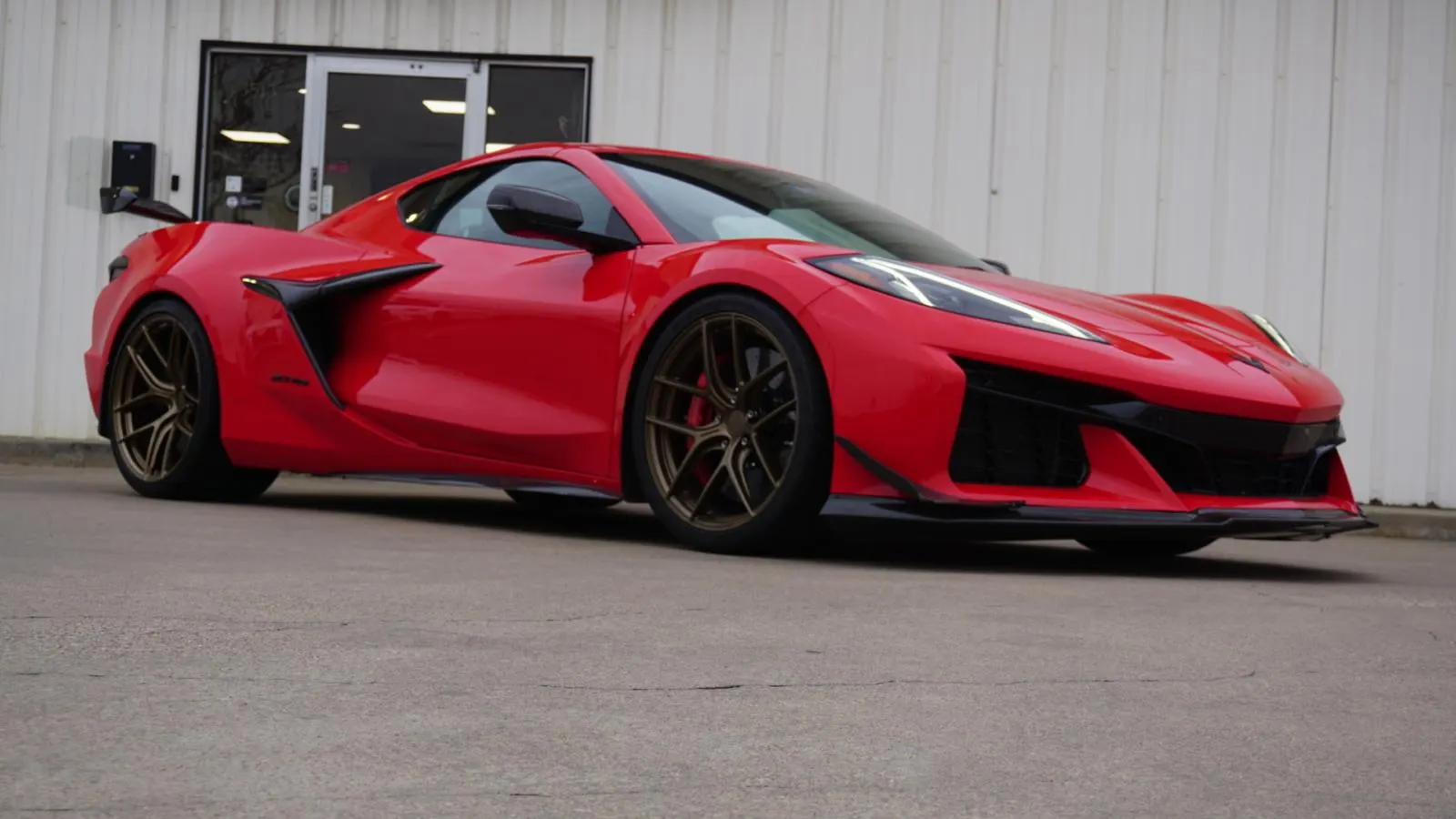 A red Chevrolet Corvette C8 Z06 with custom bronze wheels parked outside a building.