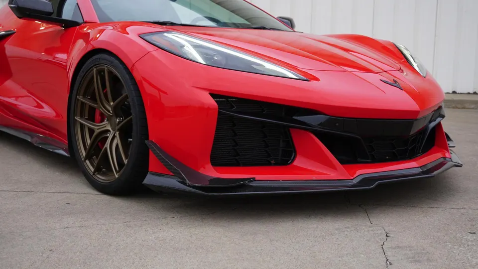 A red C8 Corvette with carbon fiber front splitter and bronze aftermarket wheels parked on concrete.
