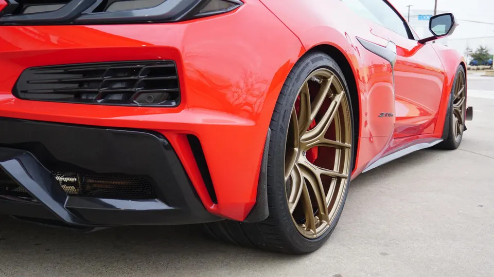 Red Corvette C8 Z06 with custom bronze multi-spoke wheels and black rear diffuser, parked outdoors.