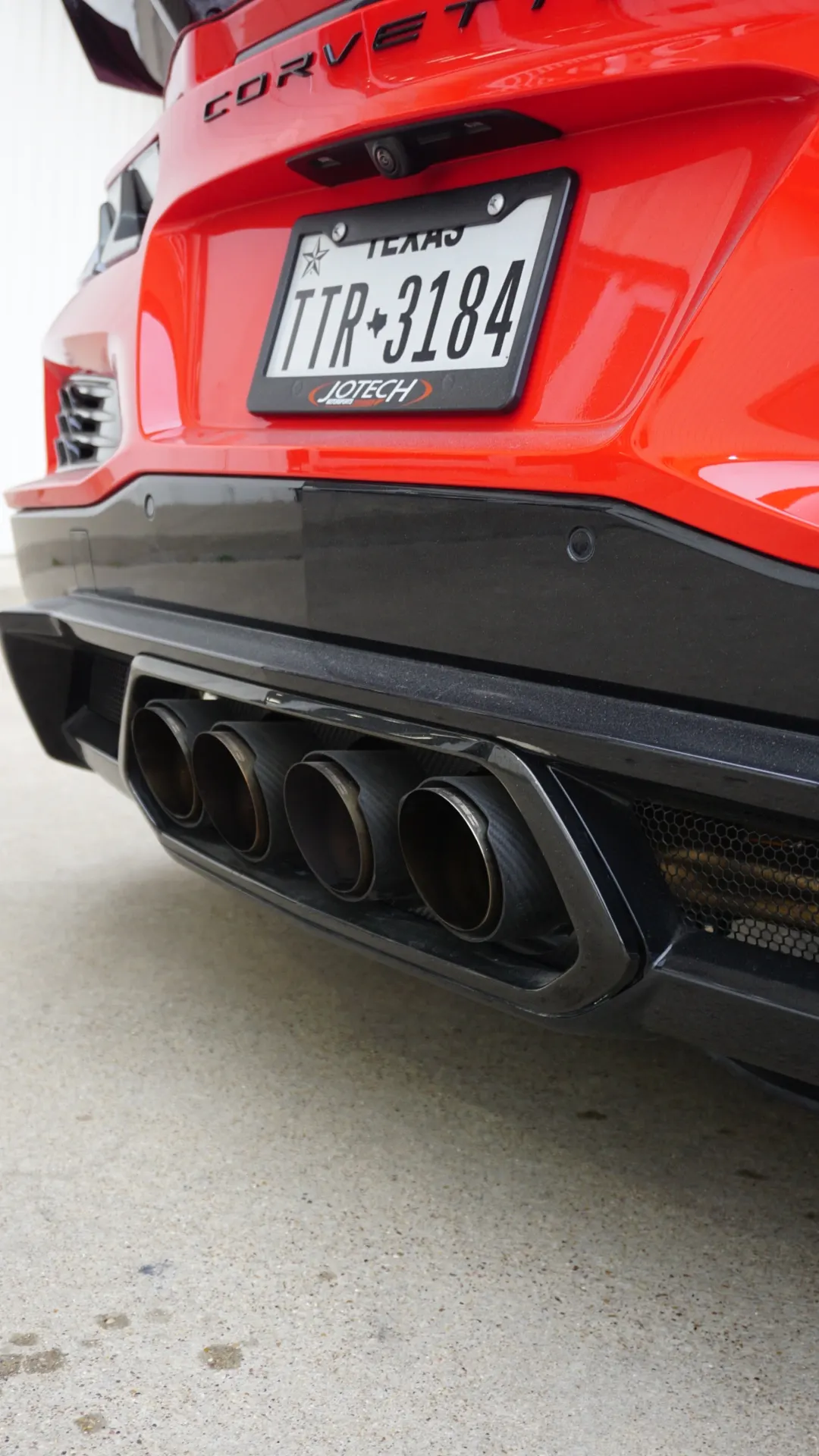 Rear view of a red C8 Corvette showing quad exhaust tips, black diffuser, and a Texas license plate.