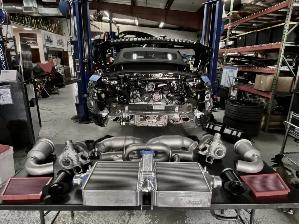 A BMW M car on a lift in a performance shop, with new turbochargers, intercoolers, and induction parts on a table.