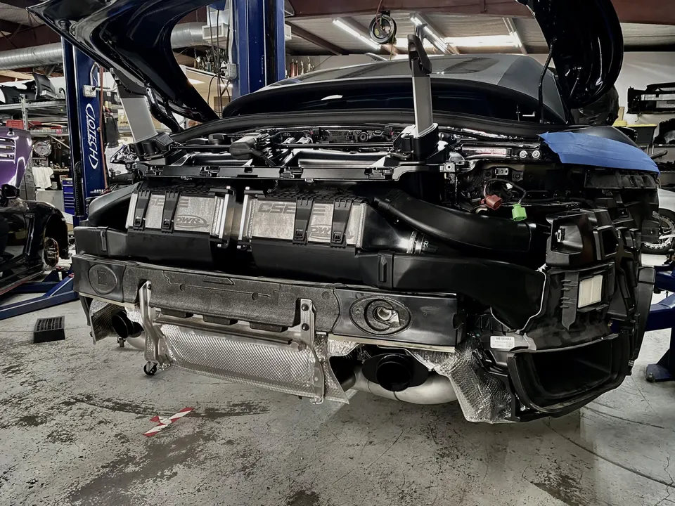 A McLaren 720S undergoing a performance upgrade in a shop, with the front bumper removed to reveal PWR intercoolers.
