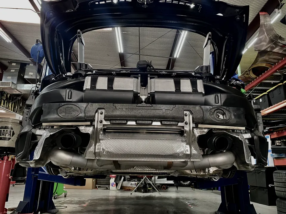 A Porsche 911 on a lift in a shop, with its rear bumper removed, showcasing the aftermarket exhaust system.