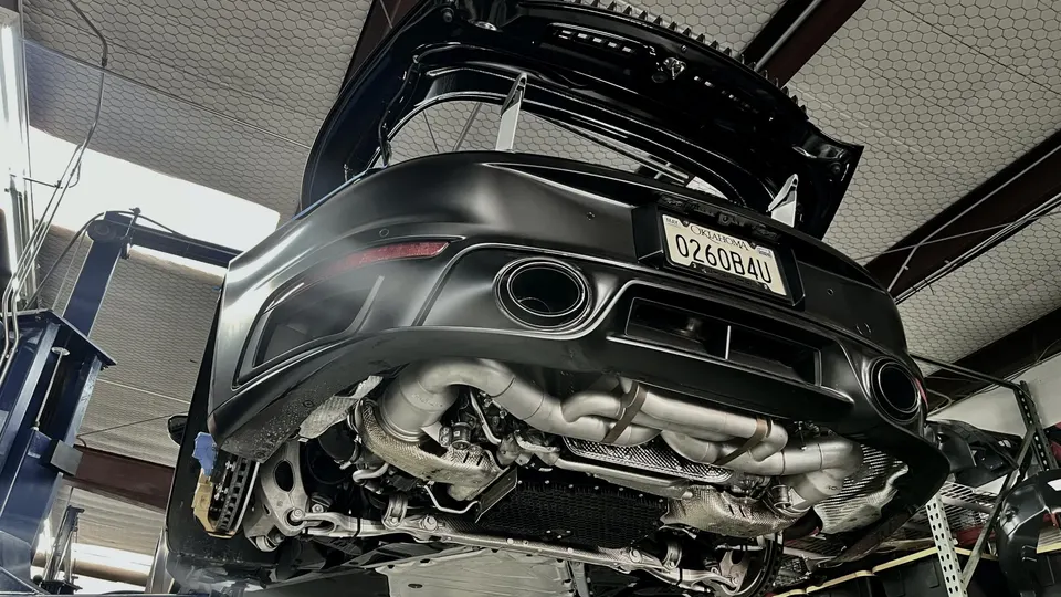 Rear view of an Audi R8 on a lift in a shop, showcasing its aftermarket exhaust system and undercarriage.