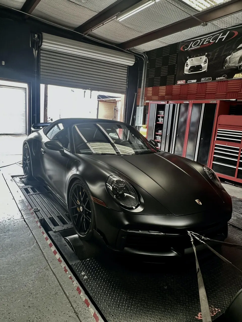 Matte black Porsche 911 GT3 strapped to a dynamometer at Jotech Motorsports for performance tuning.