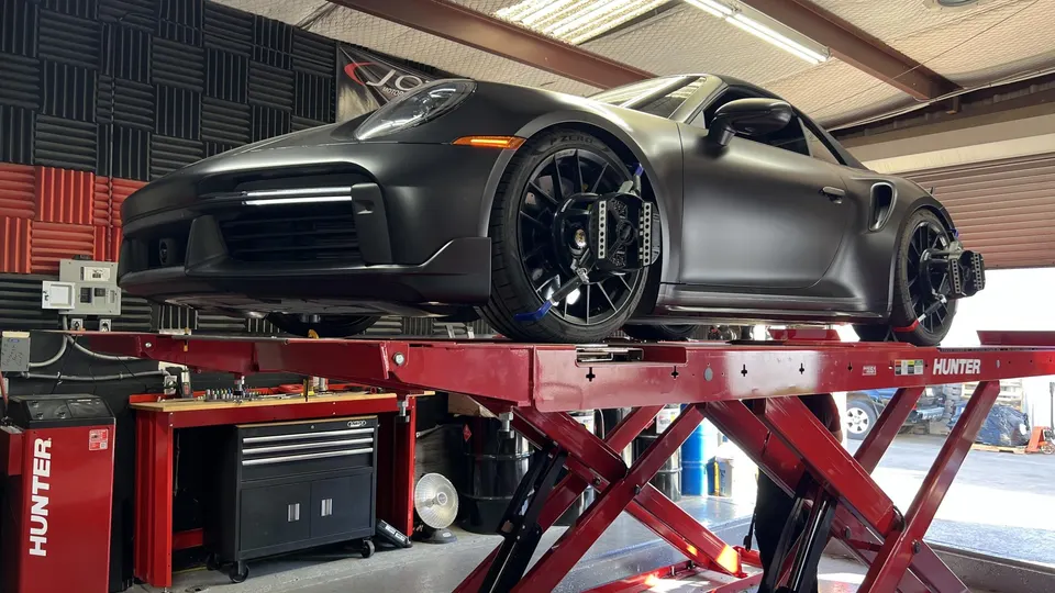 Matte black Porsche 911 on a red scissor lift with alignment sensors attached to the wheels in a performance shop.