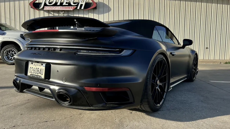 Matte black Porsche 911 convertible with a large rear wing and aftermarket exhaust tips parked outside Jotech Motorsports.