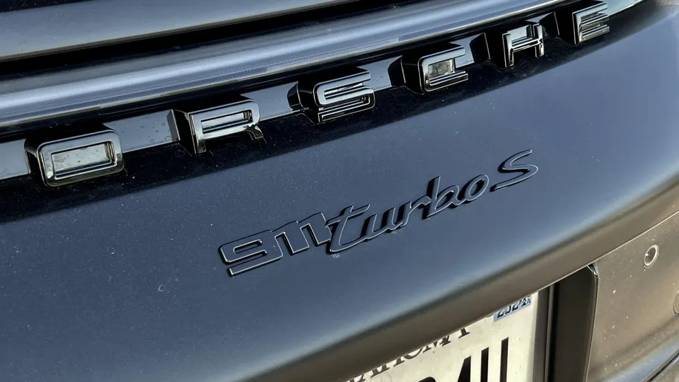 Close-up of the black Porsche and 911 turbo S emblems on the rear of a black Porsche sports car.