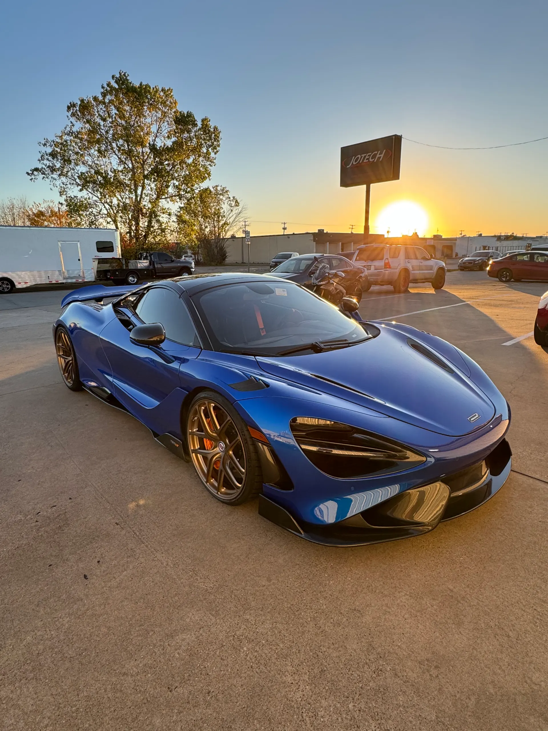 Blue McLaren 720S parked at Jotech Motorsports during sunset, showcasing its sleek design and custom bronze wheels.