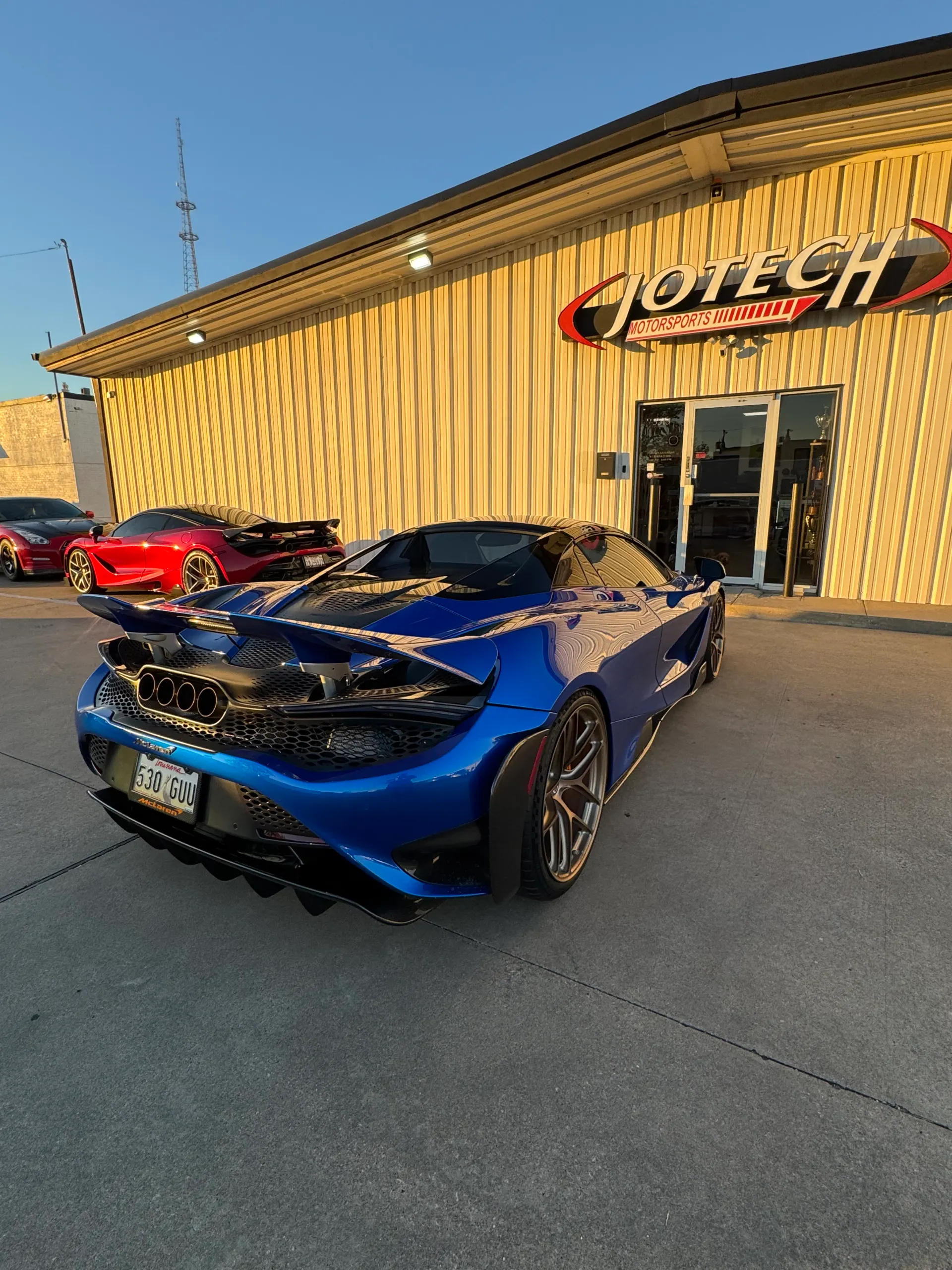 A blue McLaren 720S parked outside Jotech Motorsports, showcasing its rear diffuser and active wing.