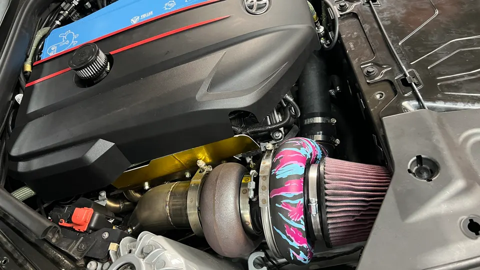 A close-up of a modified Toyota Supra B58 engine bay featuring a large aftermarket turbocharger and air intake.