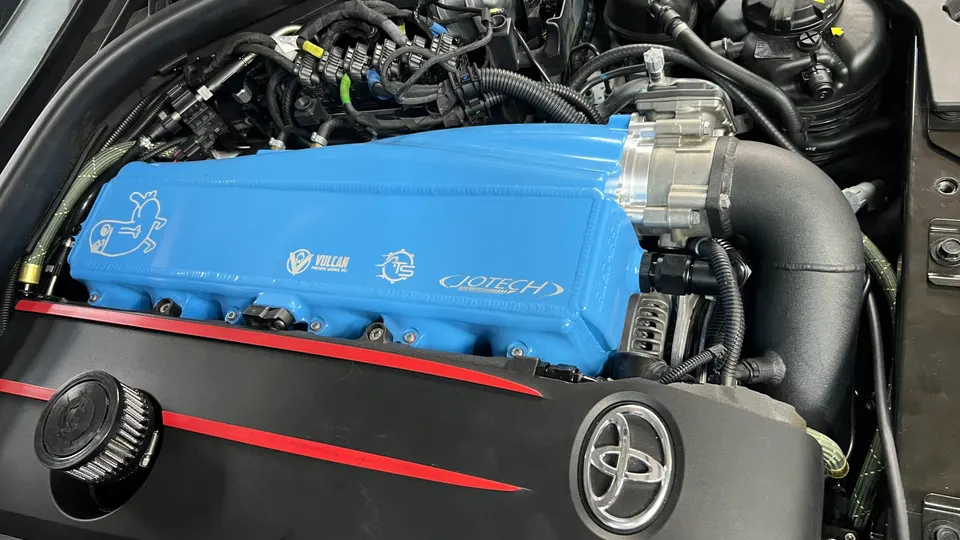A close-up of a custom blue intake manifold and engine bay in a Toyota Supra, featuring Jotech branding.