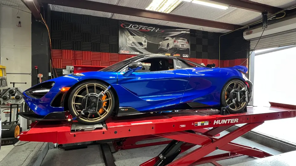 A blue McLaren supercar on a red Hunter alignment lift in a Jotech Motorsports performance tuning shop.