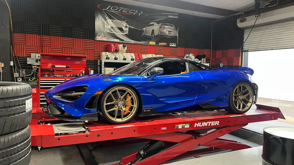 A blue McLaren 720S with gold wheels on a red Hunter lift inside a performance tuning shop.