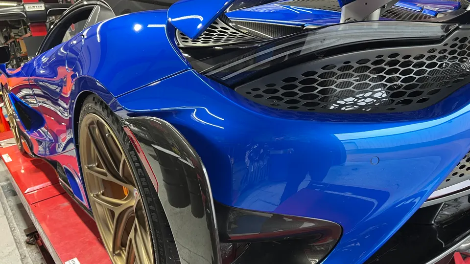 Blue McLaren supercar with gold wheels and carbon fiber rear fender on a shop lift.