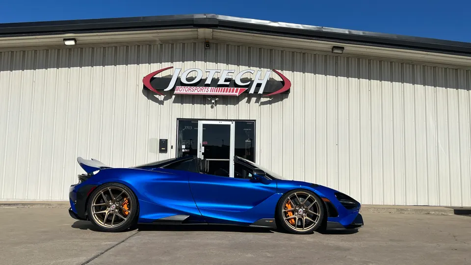 A blue McLaren 720S convertible with custom bronze wheels and orange brake calipers parked in front of Jotech Motorsports.