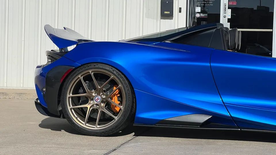 Blue McLaren 720S with bronze HRE wheels, orange brake calipers, and carbon fiber rear aero parked outside.